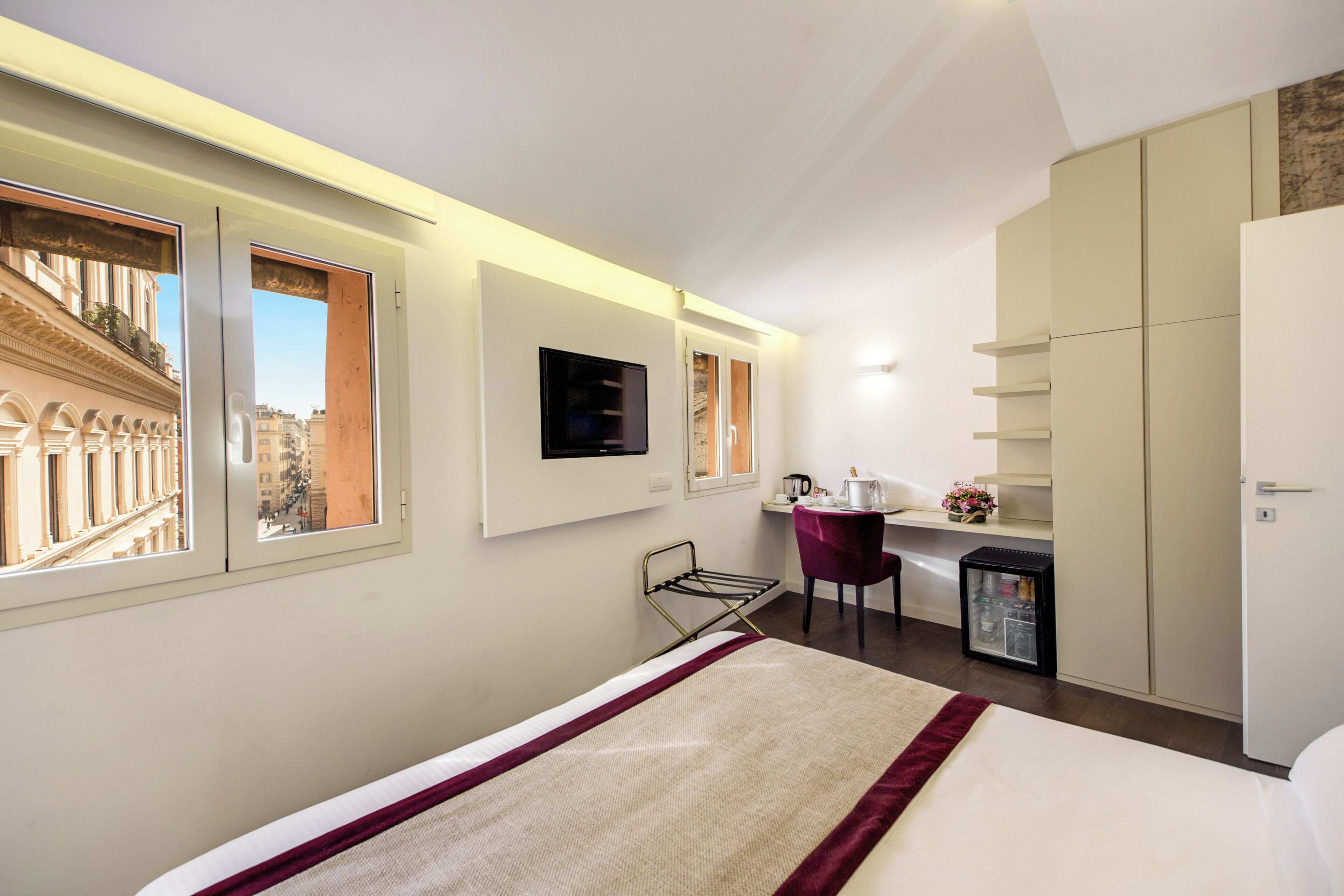A hotel room with a bed, a desk, a chair, a small refrigerator, and a wardrobe.