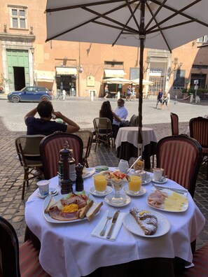An outdoor dining area with tables and chairs, a variety of breakfast dishes, and a view of the street with pedestrians and buildings in the background. - Hotel Abruzzi (Rome)