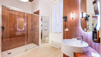 Un baño moderno con cabina de ducha de vidrio, un espejo grande y un lavamanos blanco.
