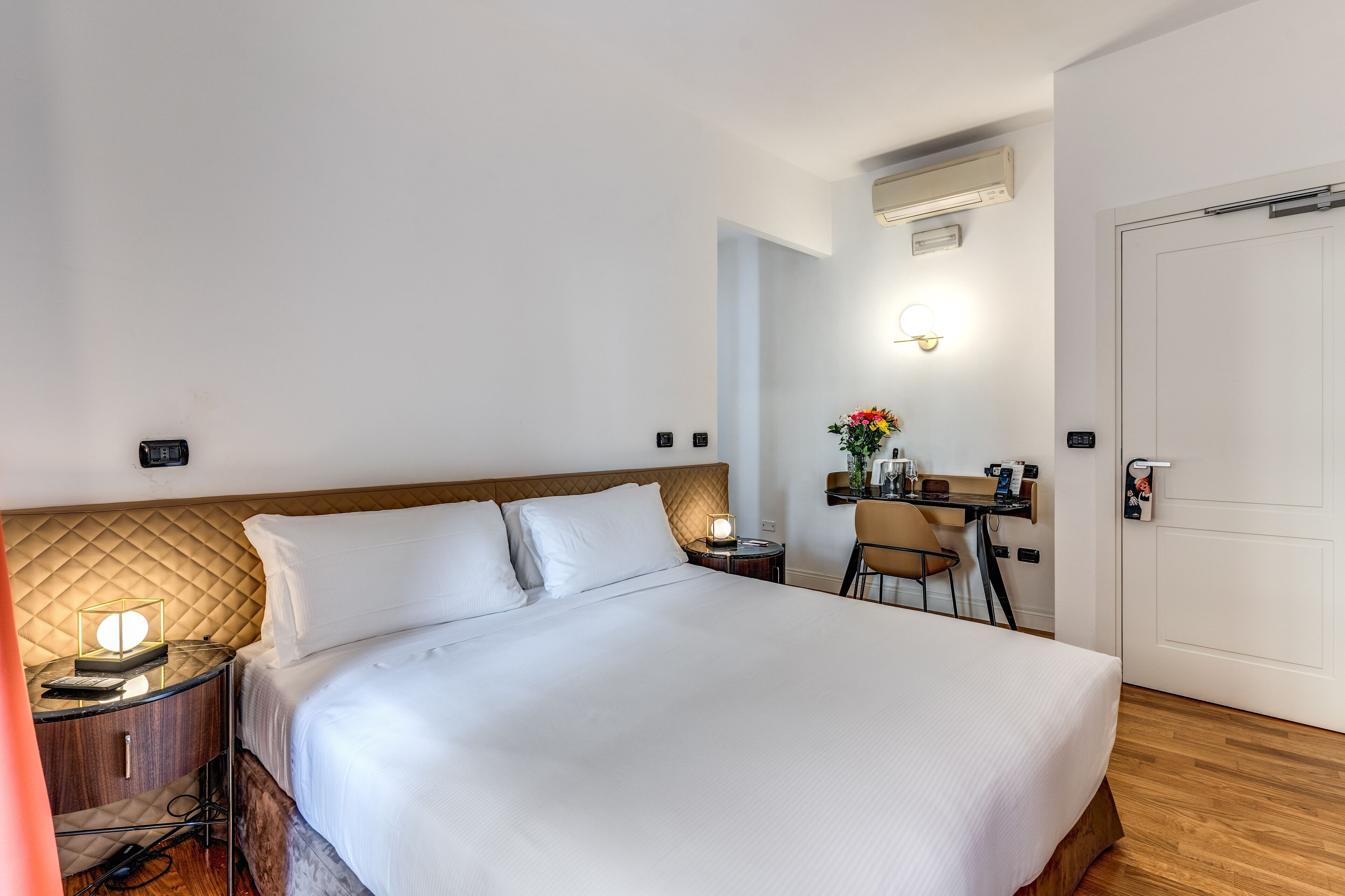 Una habitación de hotel con cama, mesita de noche, lámpara, escritorio, silla y una puerta.