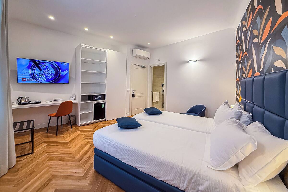 Una habitación de hotel con cama, dos sillas, un escritorio, televisión y armario.
