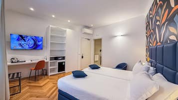 A hotel room with a bed, two chairs, a desk, a TV, and a wardrobe.