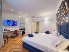 A hotel room with a bed, two chairs, a desk, a TV, and a wardrobe.