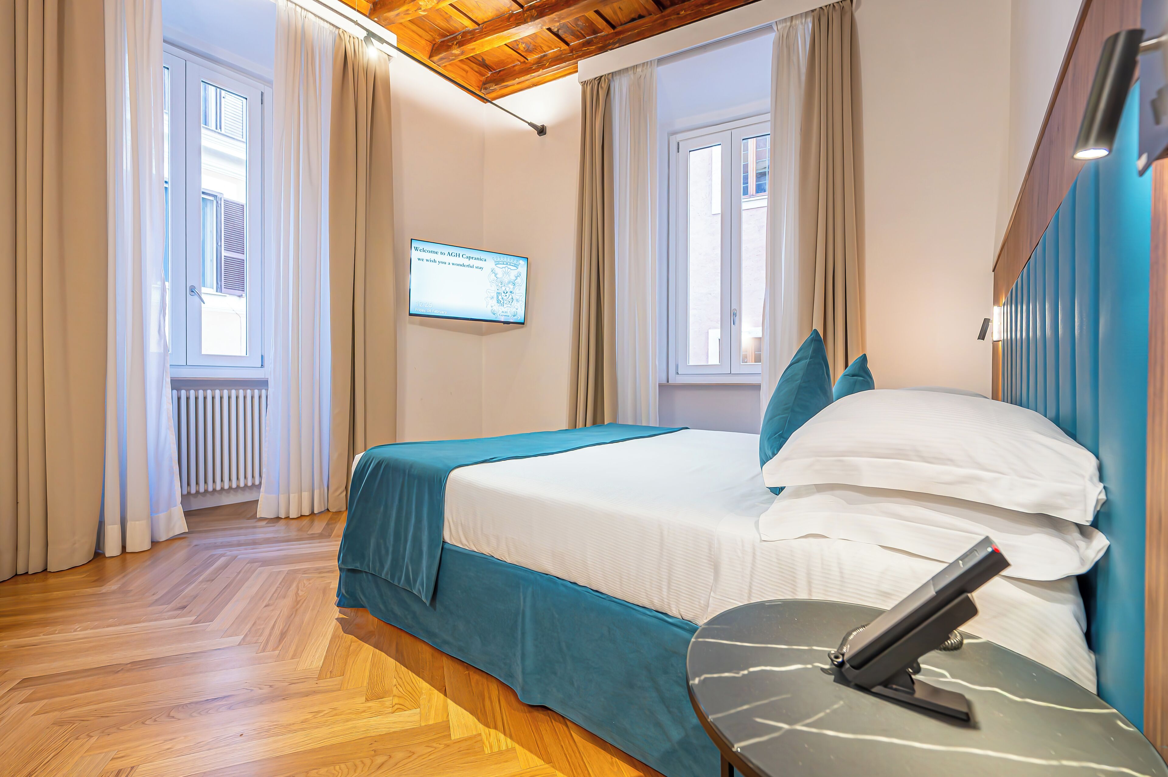 A hotel room with a bed, a desk, and a television displaying a welcome message.