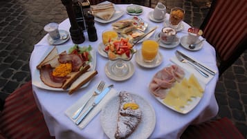 Una tavola imbandita con prodotti per la colazione, tra cui pane tostato, uova, pancetta e frutta.