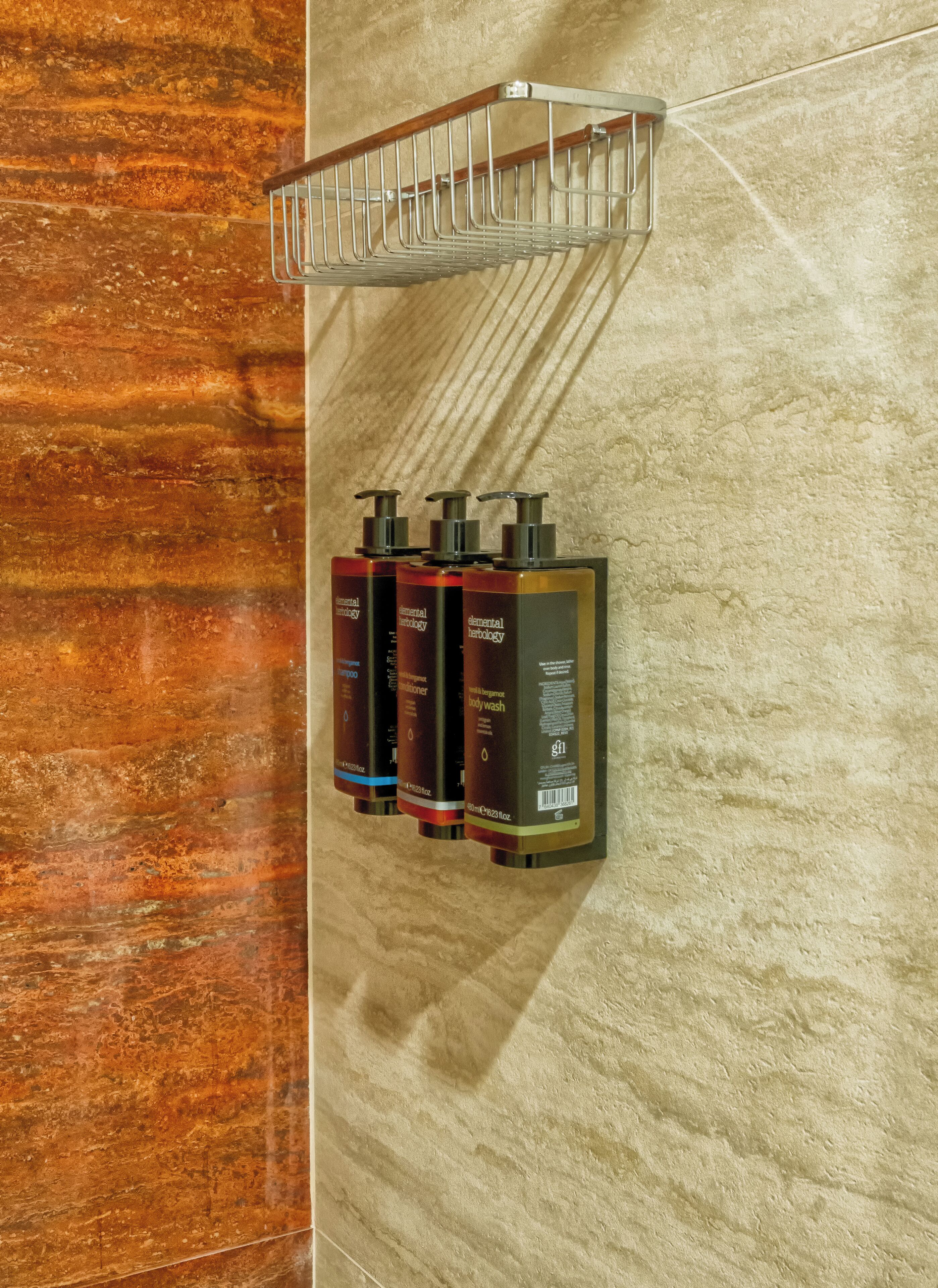 A bathroom with a marble wall, a metal towel rack, and three bottles of body wash.