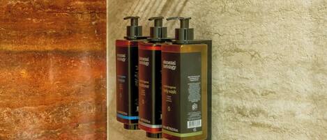A bathroom with a marble wall, a metal towel rack, and three bottles of body wash.