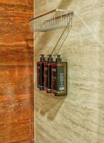 A bathroom with a marble wall, a metal towel rack, and three bottles of body wash.