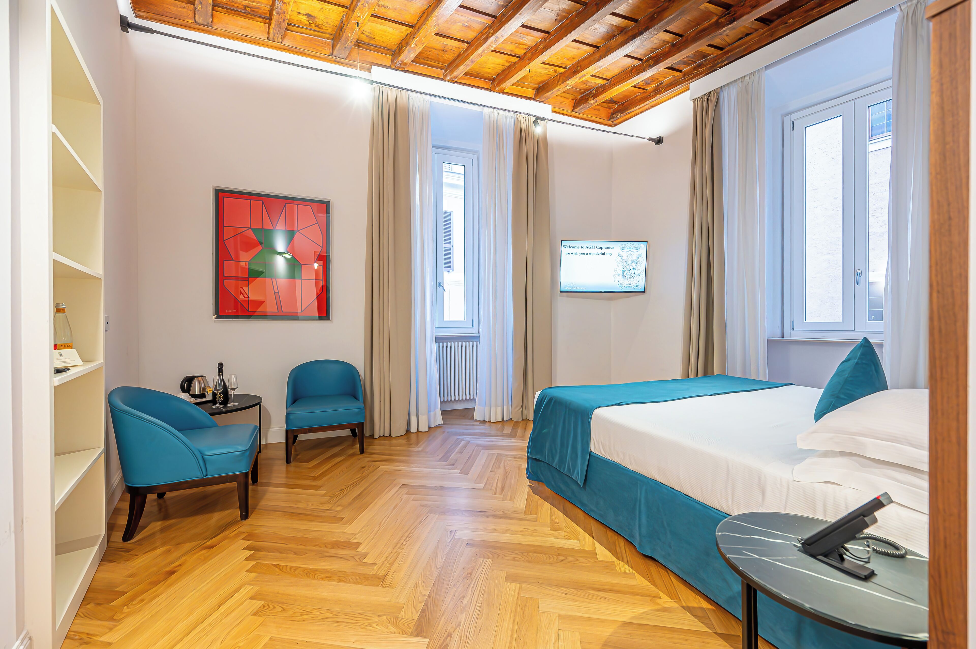 Una habitación de hotel con techo de madera, una cama con ropa de cama azul, un escritorio con teléfono y un televisor montado en la pared.