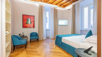 Una habitación de hotel con techo de madera, una cama con ropa de cama azul, un escritorio con teléfono y un televisor montado en la pared.