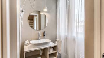 Une salle de bain moderne avec un miroir rond, un lavabo blanc, un porte-serviettes et un porte-rouleau de papier toilette.