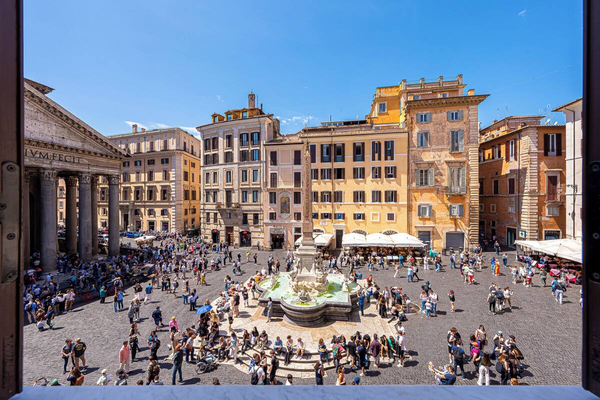 Una plaza pública animada con edificios históricos, una fuente central y zonas de estar al aire libre.