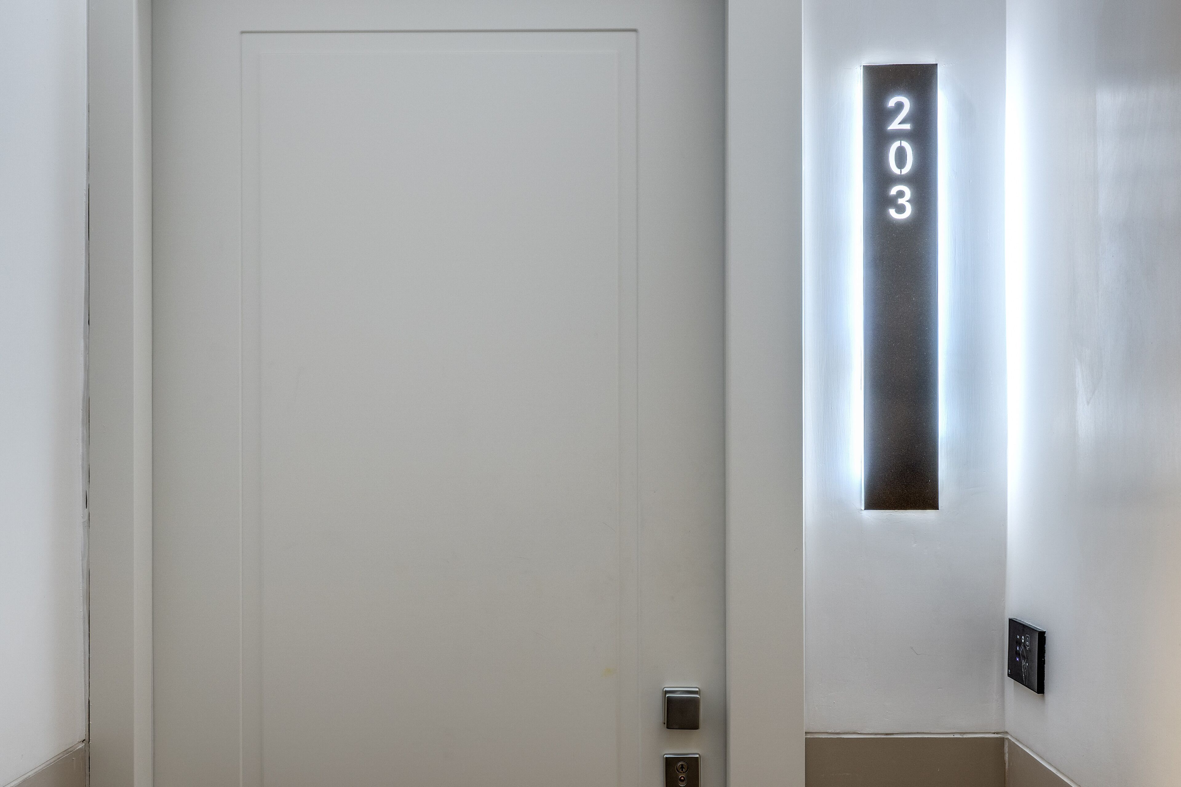 A white door with a number plate displaying "203" and a wall-mounted light fixture.