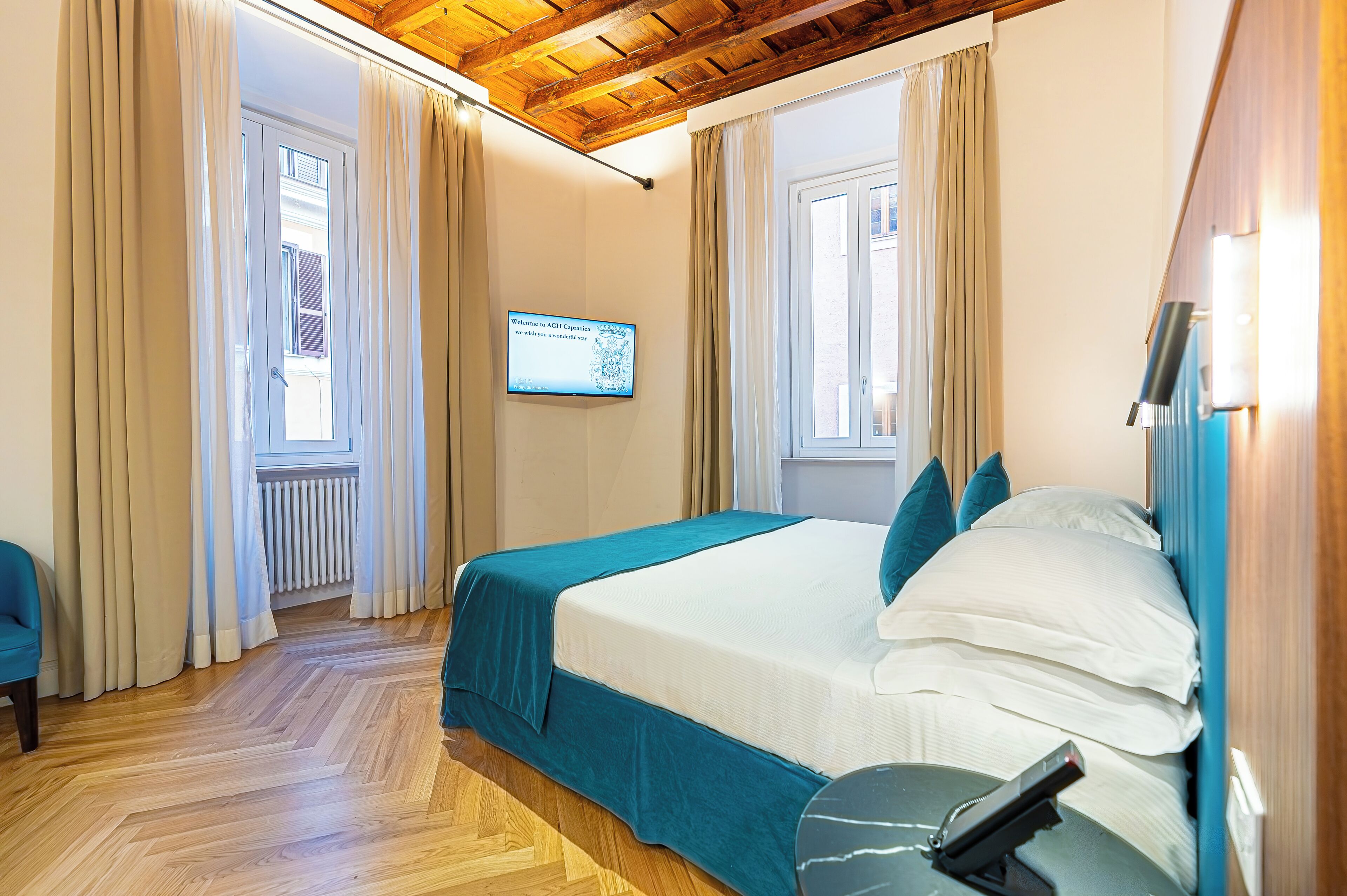 A bedroom with a bed, curtains, a television, and a wooden floor.