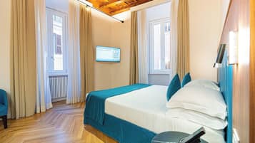 A bedroom with a bed, curtains, a television, and a wooden floor.