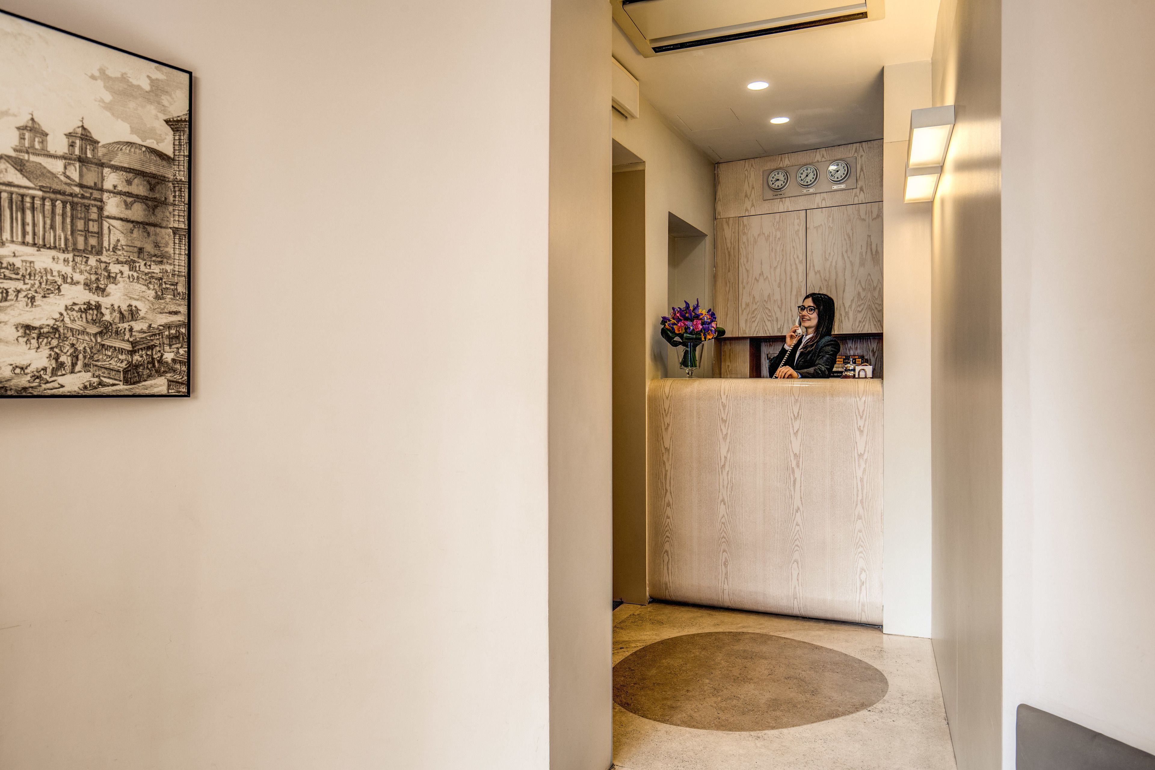 A hallway with a reception desk, a clock, and a framed artwork on the wall.
