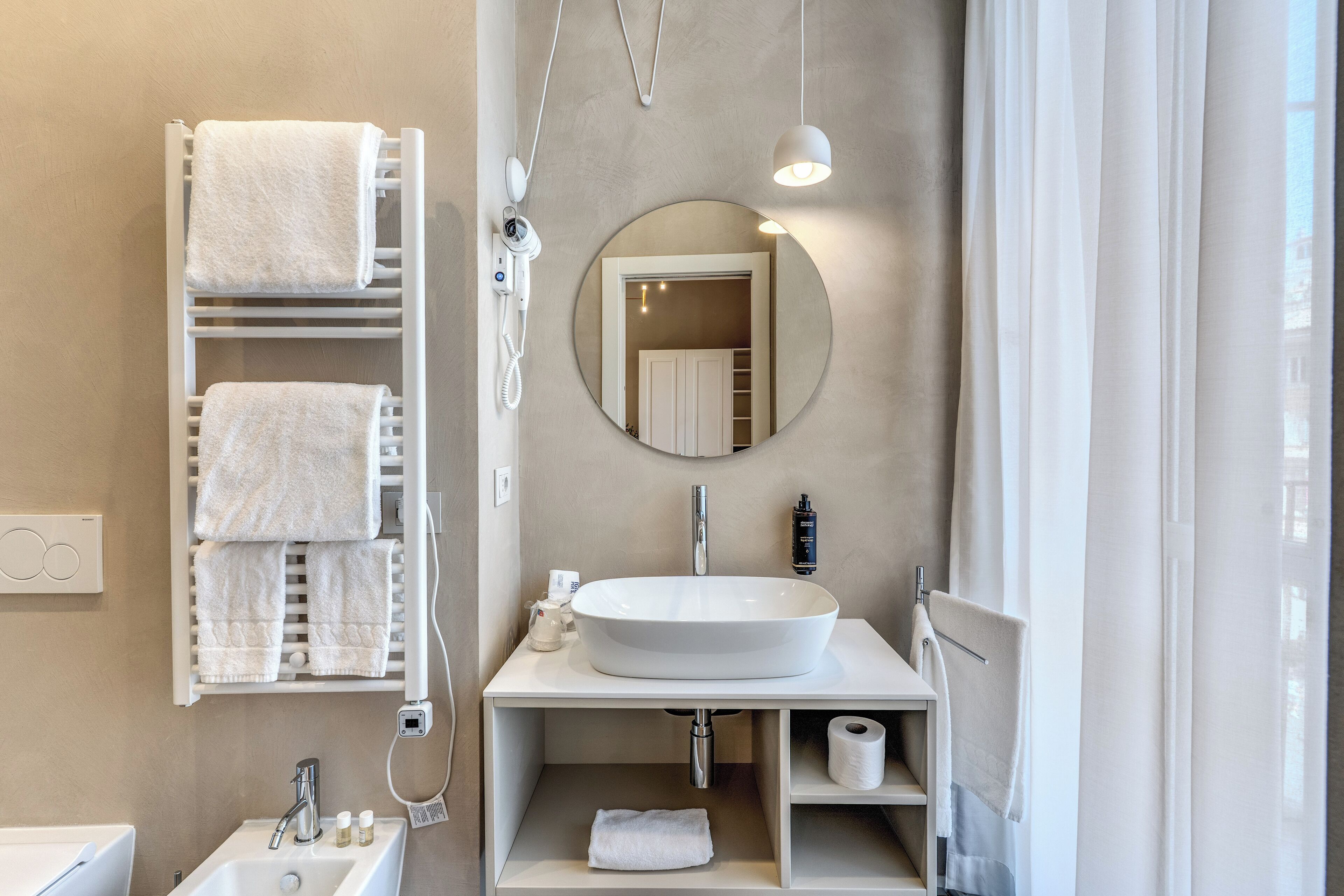 Un baño moderno con un lavamanos grande, un espejo y un perchero con varias toallas.