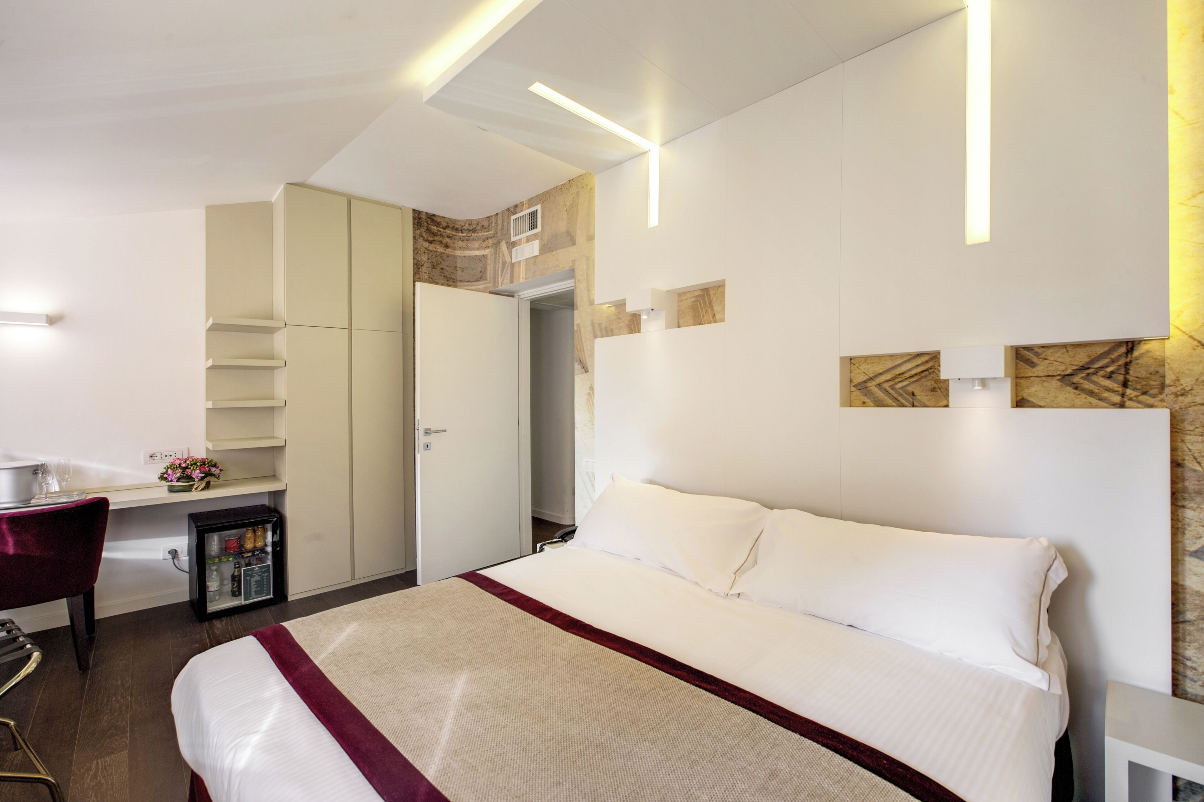 A hotel room with a bed, a desk, a minibar, and a wardrobe.