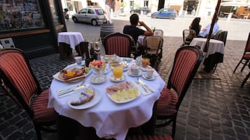 Un caffè all'aperto con tavoli apparecchiati per la colazione, con piatti di cibo, bevande e una vista della strada sullo sfondo.