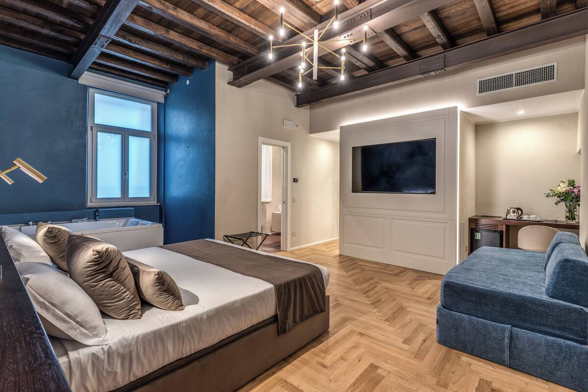Un dormitorio moderno con una cama, un sofá azul, un televisor y un techo de madera.