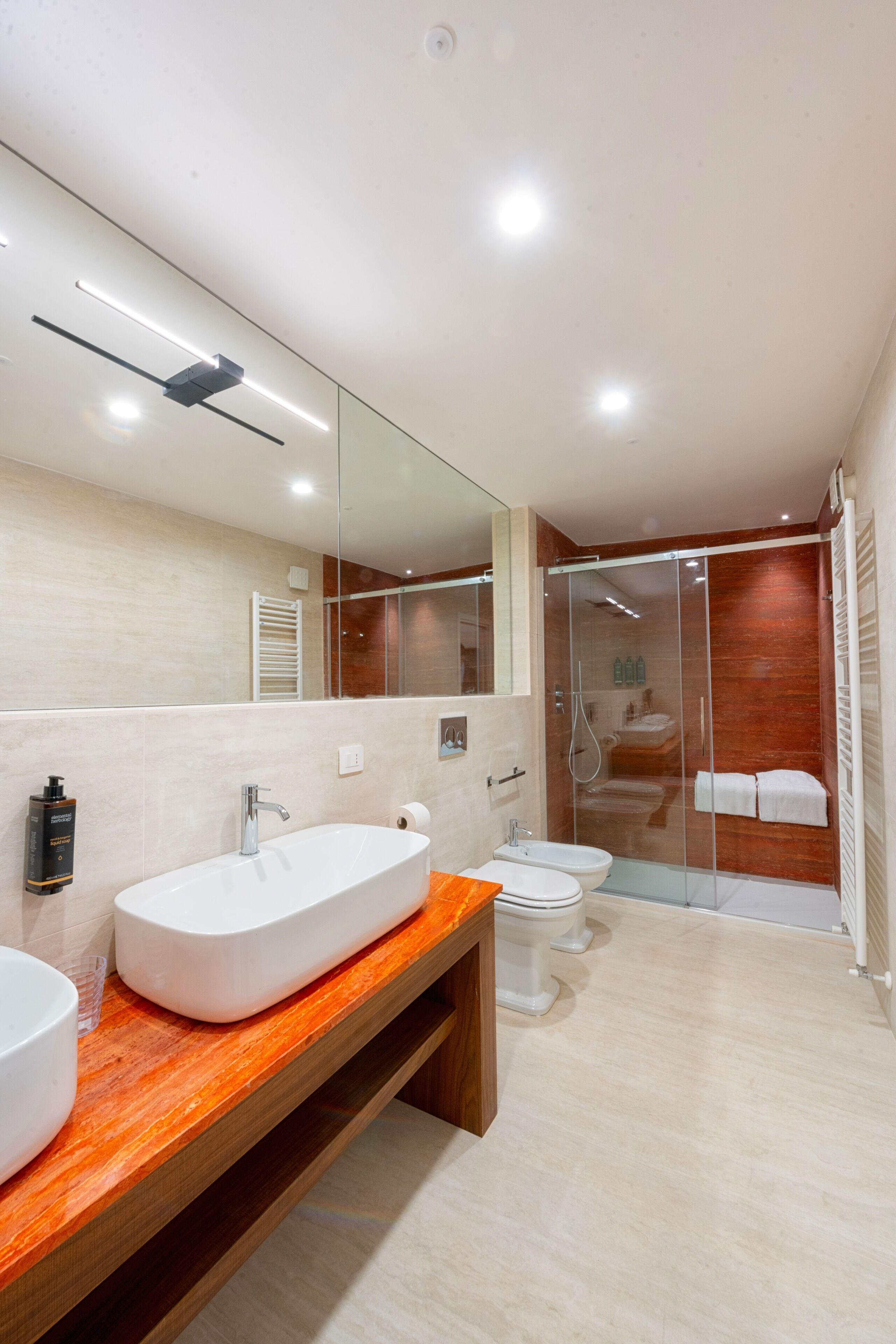 A modern bathroom with a large mirror, two sinks, a shower, and a glass-enclosed shower area.