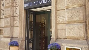 Exterior do Hotel Altavilla, com fachada clássica, entrada imponente e dois grandes vasos de flores na entrada.