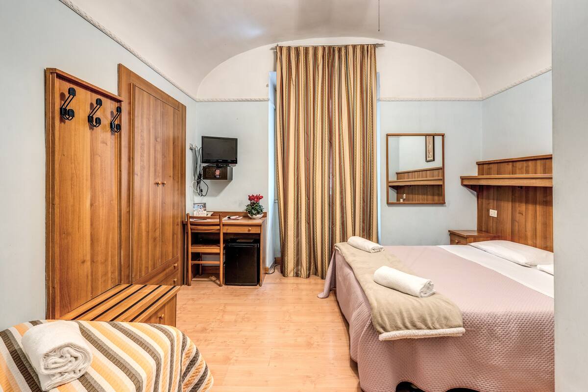 A hotel room with a bed, a desk, a wardrobe, a mirror, and a TV.