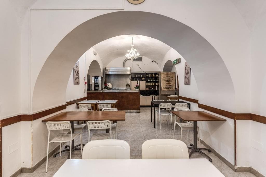 Un ristorante con cucina centrale, sedie bianche e un lampadario.