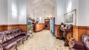 Um hall de entrada com piso de mármore, sofás de couro, balcão de recepção e um quadro na parede.