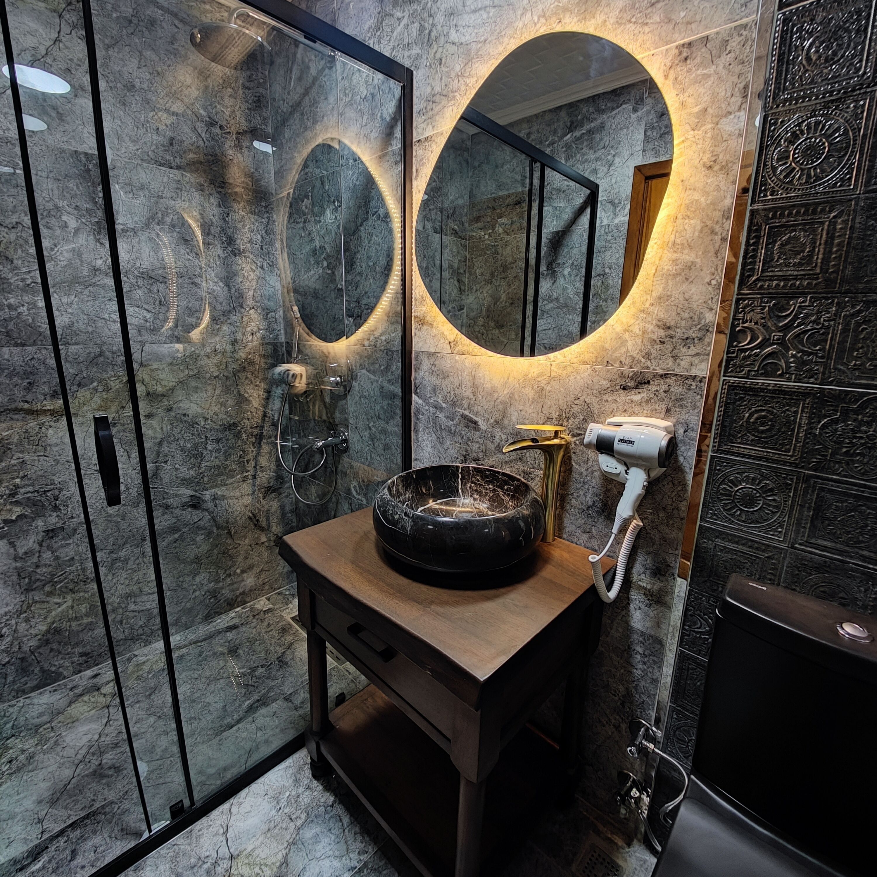A bathroom with a marble vanity, a round mirror, and a hairdryer on the counter.