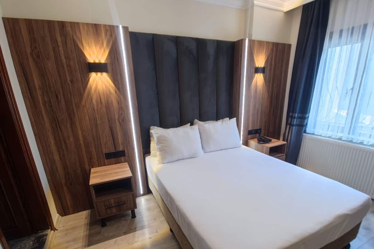 A hotel room with a large bed, wooden panel walls, and two bedside tables with lamps.