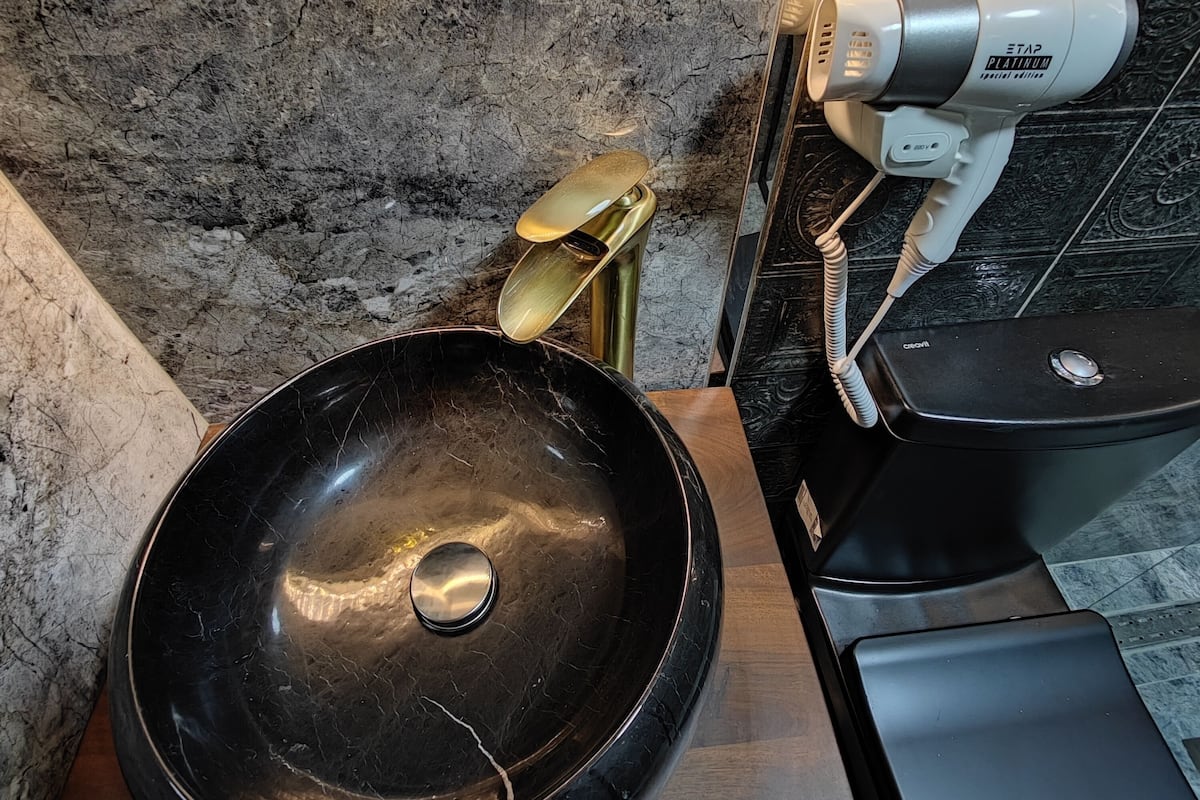 A bathroom with a black marble sink, a gold-colored faucet, and a white hairdryer on a vanity.