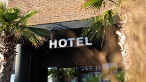L’entrée d’un hôtel, avec une façade en briques, un auvent et des plantes en pot.