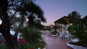 An outdoor patio with white chairs and tables, surrounded by plants and a wooden pergola. - Hotel Ninays (Lloret de Mar)