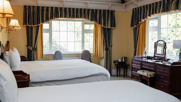 A hotel room with two beds, a desk, a chair, a dresser, and a window with curtains.
