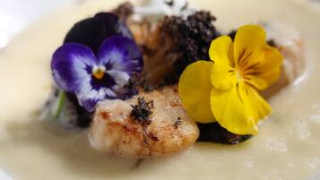 A dish with a creamy sauce, a piece of fish, and edible flowers.