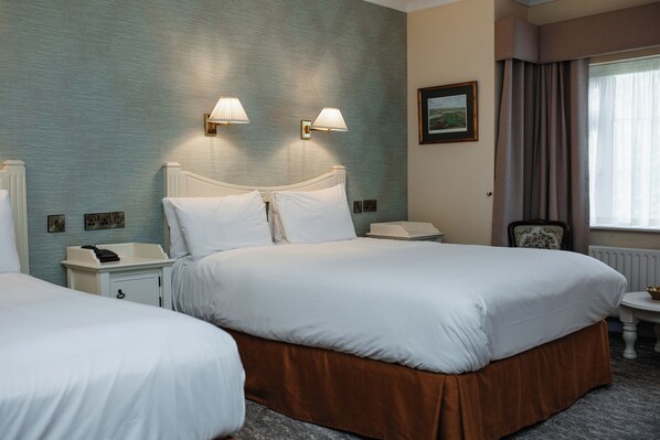 A hotel room with two beds, bedside lamps, a nightstand, a chair, and a window with curtains. - Killeen House Hotel (Killarney)