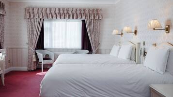 Ett hotellrum med två sängar, ett fönster med gardiner, en stol och väggmonterade lampor.