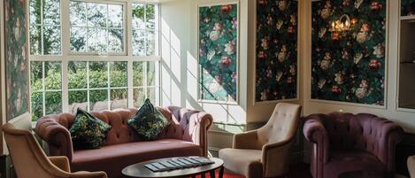 A room with a red carpet, a sofa, two armchairs, a coffee table, and floral wallpaper.