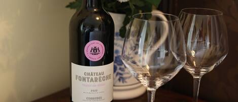 A bottle of Chateau Fontareche 2022 wine and two empty wine glasses on a wooden table.