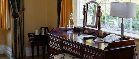 A room with a wooden dresser, a mirror, a lamp, and a window with curtains.