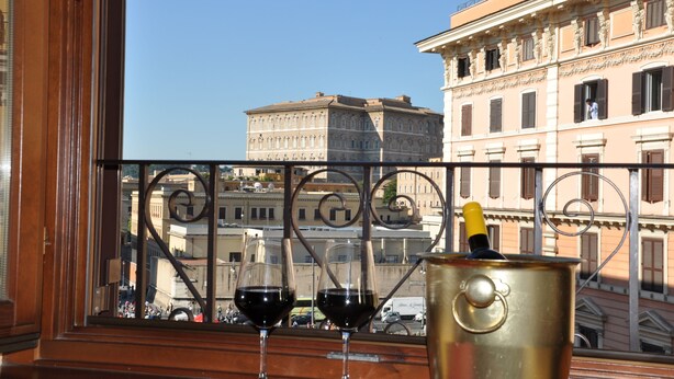 A balcony with two wine glasses and a champagne bottle, overlooking a historic building with classical architecture. - Le Suite di Via Ottaviano (Rome)