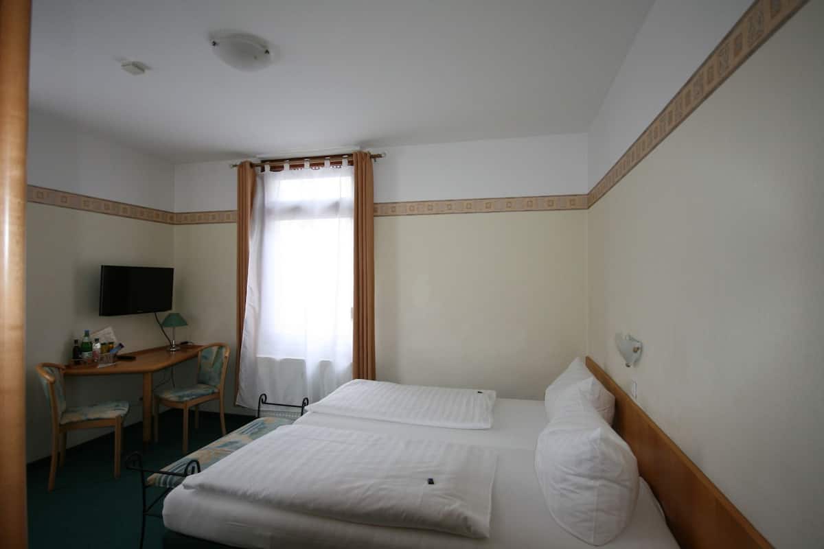 A hotel room with two beds, a desk with a chair, a television, and a window with curtains.