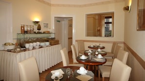 A dining area with a buffet, round tables with chairs, and a mirror on the wall. - Hotel Classic Inn (Heidelberg)