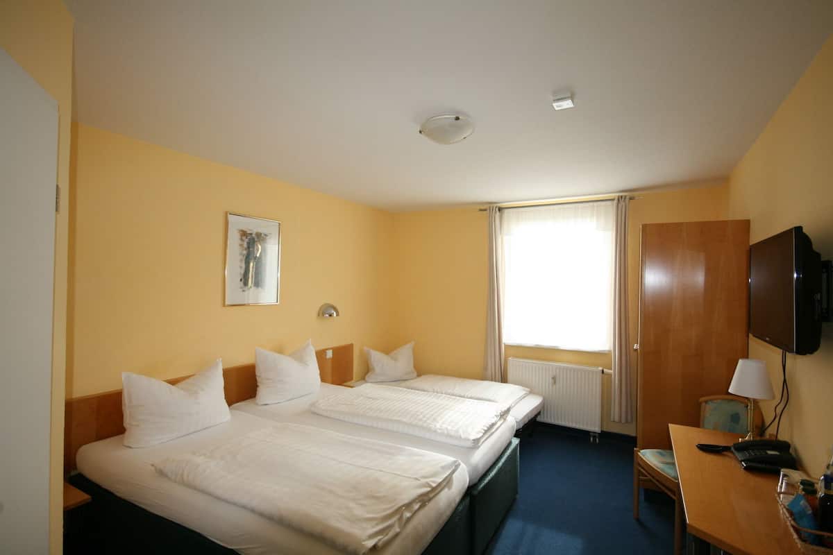 A hotel room with two beds, a desk with a chair, a television, and a window with curtains.