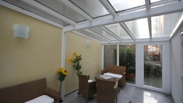 A sunlit room with a glass ceiling, wicker furniture, and a potted plant. - Hotel Classic Inn (Heidelberg)
