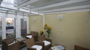 A sunlit indoor seating area with wicker furniture and a glass door leading outside. - Hotel Classic Inn (Heidelberg)