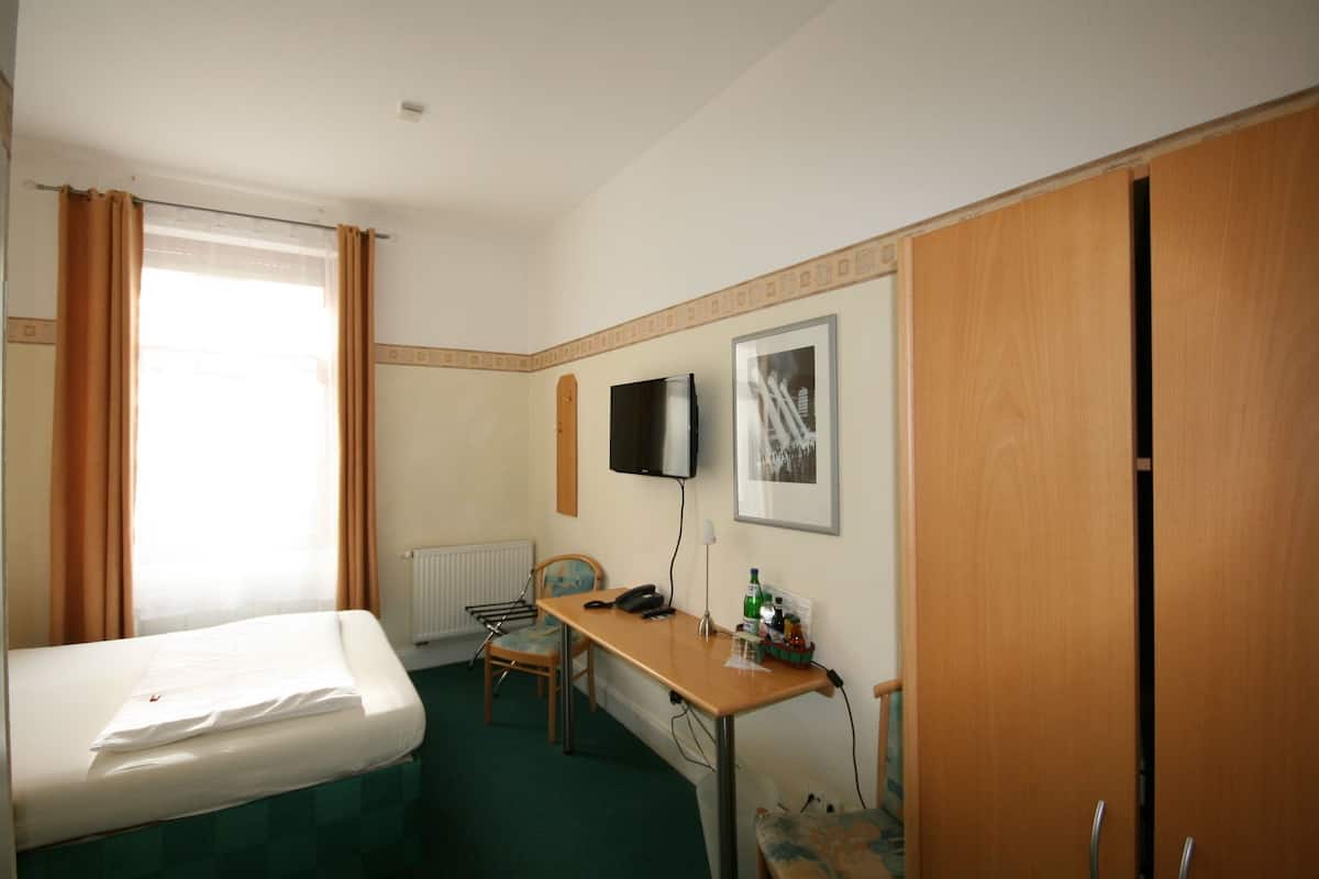 A hotel room with a bed, a desk, a chair, a radiator, a television, and a wardrobe.