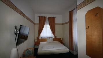 Habitación de hotel con cama, televisor en la pared, escritorio y silla, y una puerta.