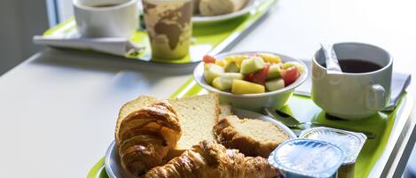 Bandeja de desayuno con cruasanes, pan, fruta, yogur y café.